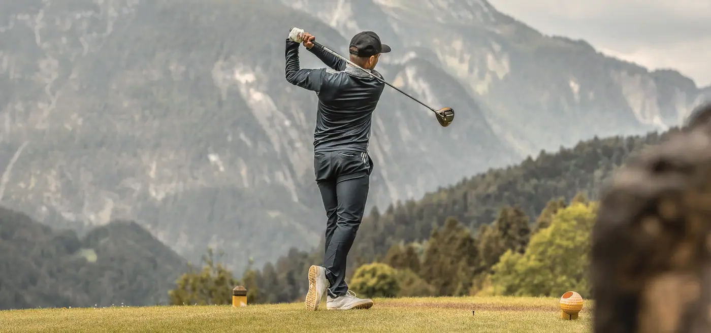 Golfer beim Abschlag vor dem Bergpanorama